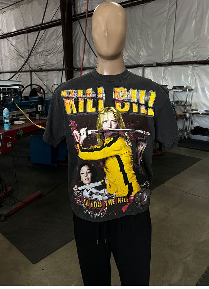 A mannequin wears a "100 Jumbo Oversized T Shirt Printing - Garment-Dyed Heavyweight Shirts with Screen Printing (17" W x 23" H) - Ideal for Oversized T-Shirt Designs - Rap Style - Premium" featuring characters from the film. The background shows an industrial workspace with various equipment and tools.